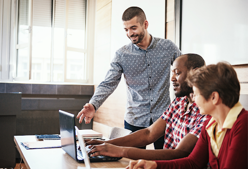 A male instructor pointing at a laptop screen while collaborating with a diverse team of employees during a technical training session.